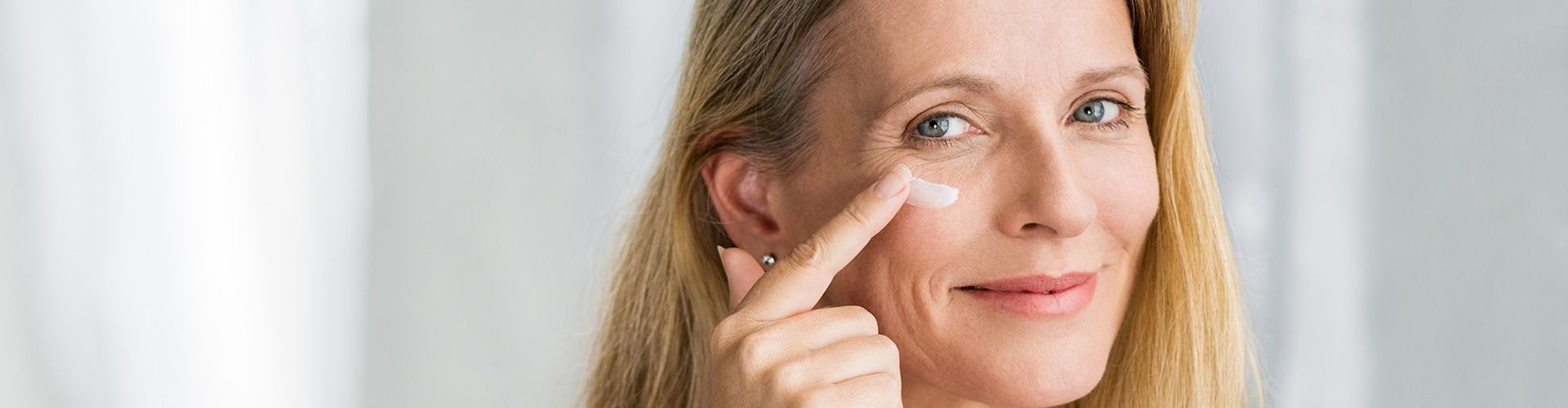 Frau schaut in den Spiegel und cremt ihr Gesicht.